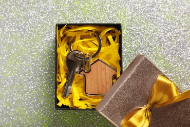 Key with trinket in shape of house, glitter and gift box on shiny surface, flat lay. Housewarming party