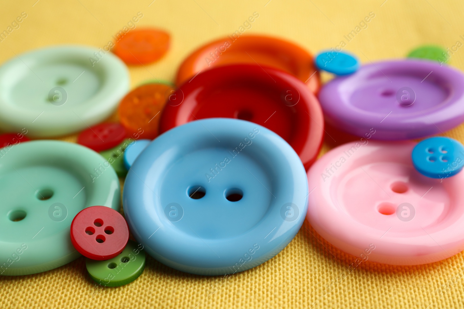 Photo of Many bright sewing buttons on yellow fabric, closeup