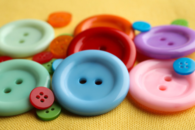 Many bright sewing buttons on yellow fabric, closeup