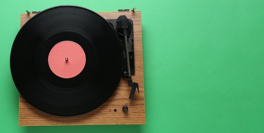 Photo of Modern turntable with vinyl record on green background, top view