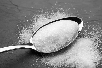 Granulated sugar and spoon on black table, closeup