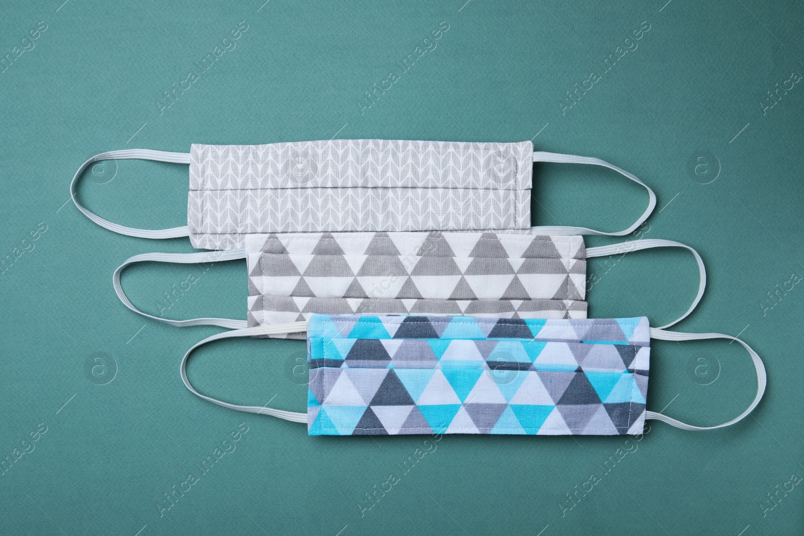 Photo of Homemade protective masks on blue-green background, flat lay. Sewing idea