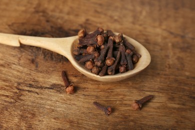 Photo of Aromatic dry cloves and spoon on wooden table, closeup