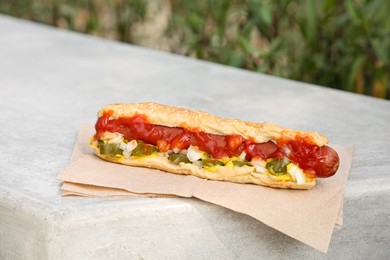Photo of Fresh tasty hot dog with ketchup on light grey parapet outdoors