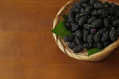 Photo of Wicker basket with delicious ripe black mulberries on wooden table, above view. Space for text