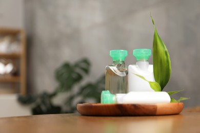 Mini bottles of cosmetic products and green branch on wooden table against blurred background. Space for text