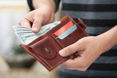 Photo of Man putting money into wallet on blurred background, closeup