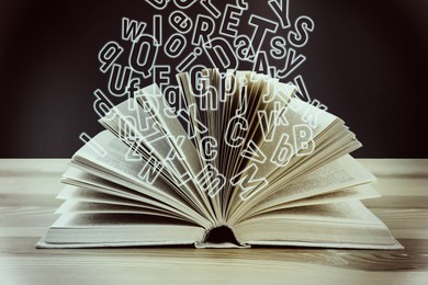 Image of Open book with flying letters on wooden table. Dyslexia concept