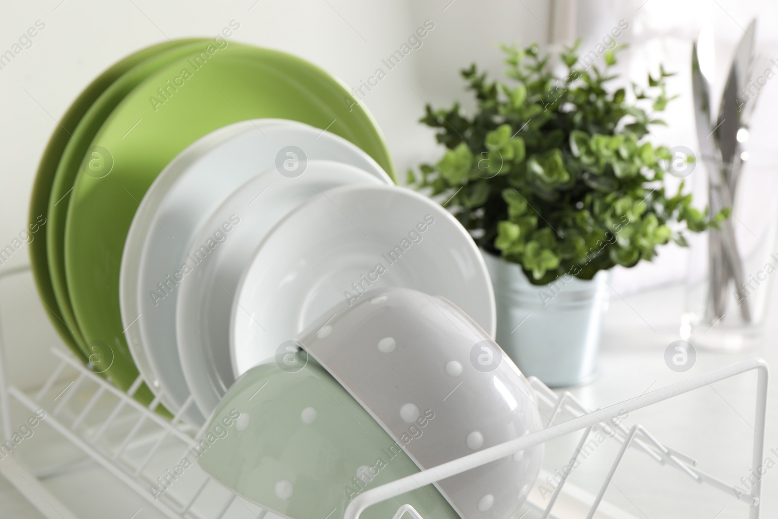 Photo of Drainer with different clean dishware and houseplant on light table in kitchen