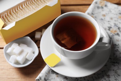 Photo of Tea bags package, sugar and cuphot drink on wooden table, closeup
