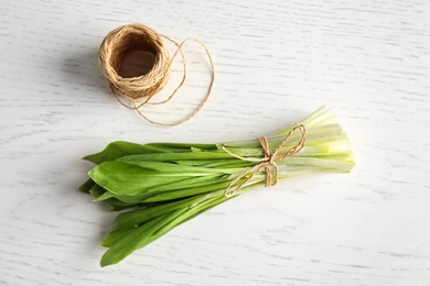 Photo of Bunch of wild garlic or ramson and thread on wooden table, top view