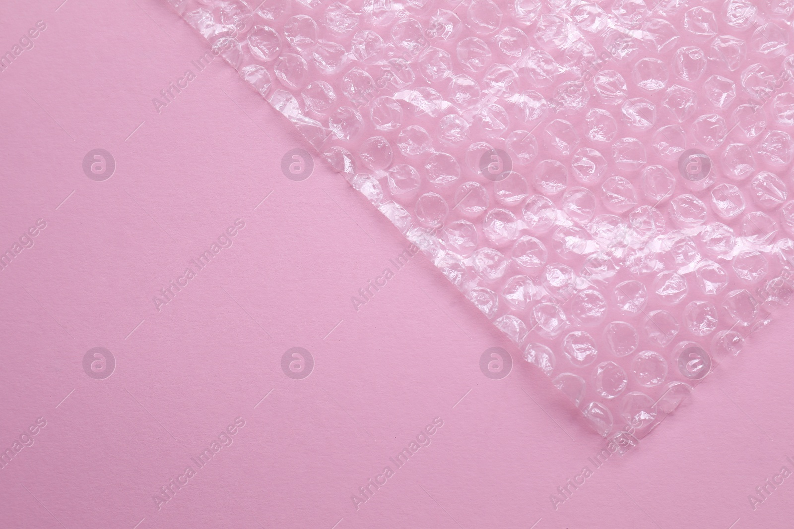 Photo of Transparent bubble wrap on pink background, top view. Space for text