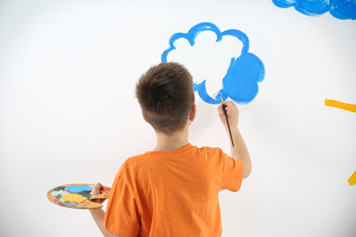 Photo of Little child painting cloud on white wall in room