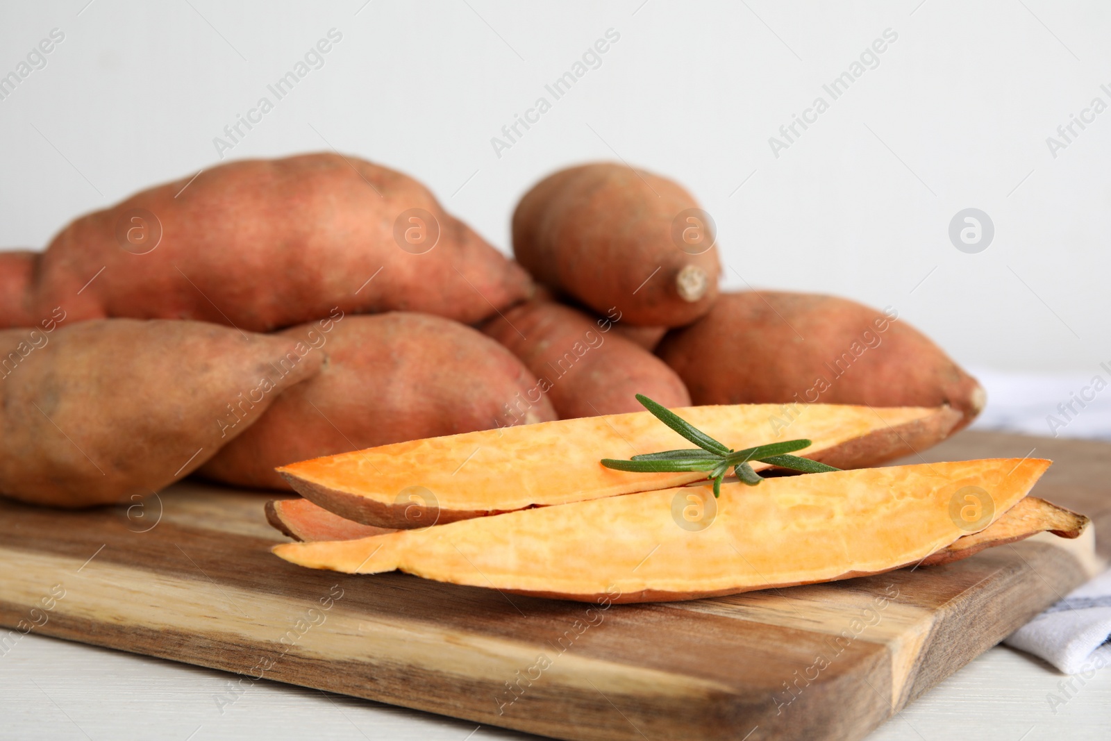 Photo of Wooden board with cut and whole sweet potatoes on white table, closeup