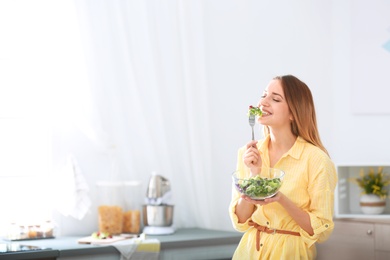 Happy young woman eating salad in kitchen, space for text. Healthy diet