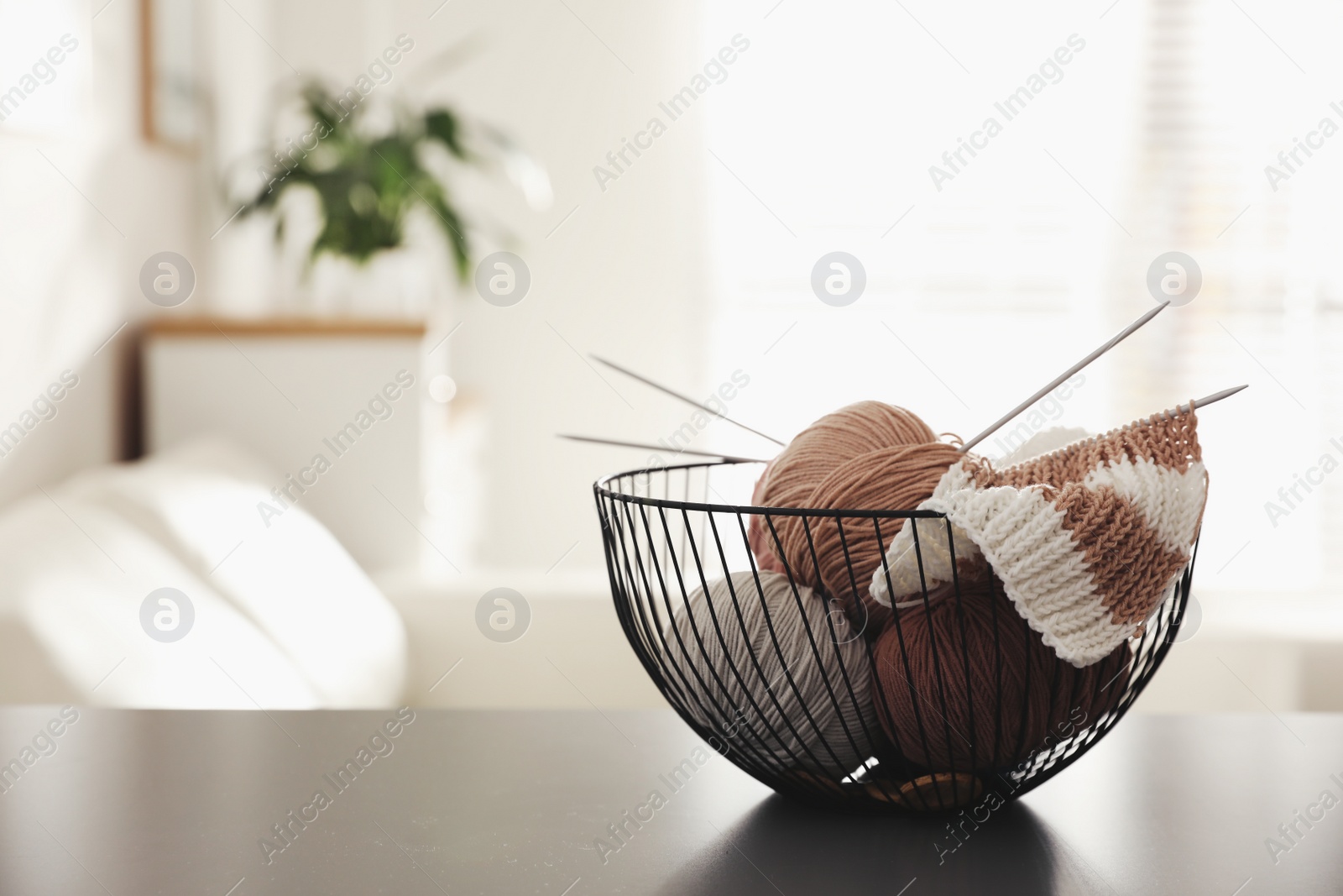 Photo of Yarn balls and knitting needles in metal basket on grey table indoors, space for text. Creative hobby