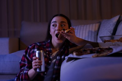 Young woman eating pizza while watching TV in room at night. Bad habit