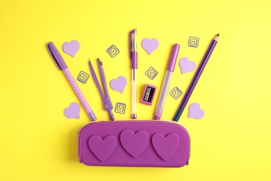 Photo of Purple pencil case and stationery on yellow background, flat lay