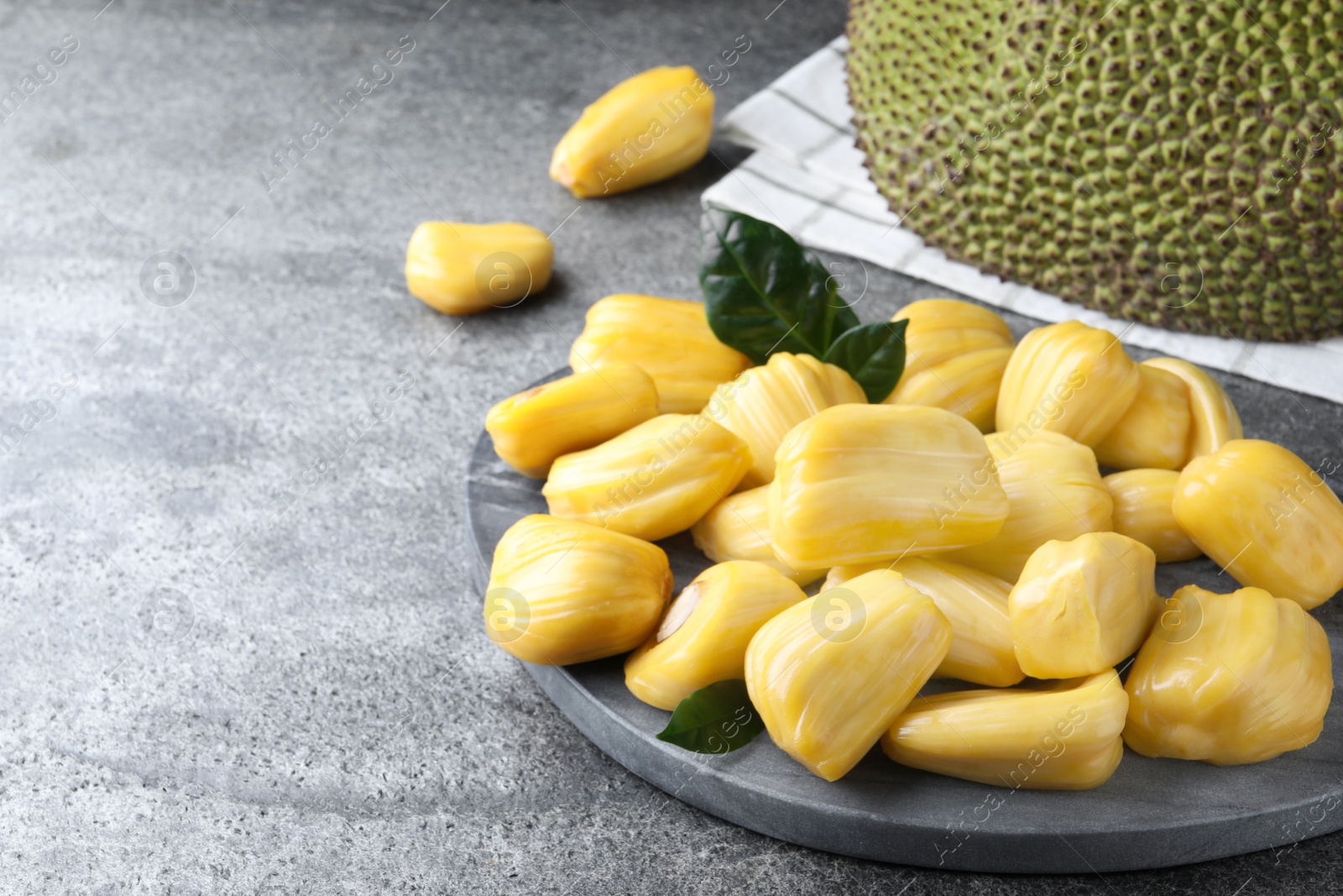 Photo of Fresh exotic jackfruit bulbs on grey table. Space for text