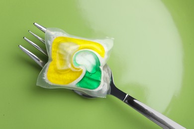 Photo of Green plate with fork and dishwasher detergent pod, top view