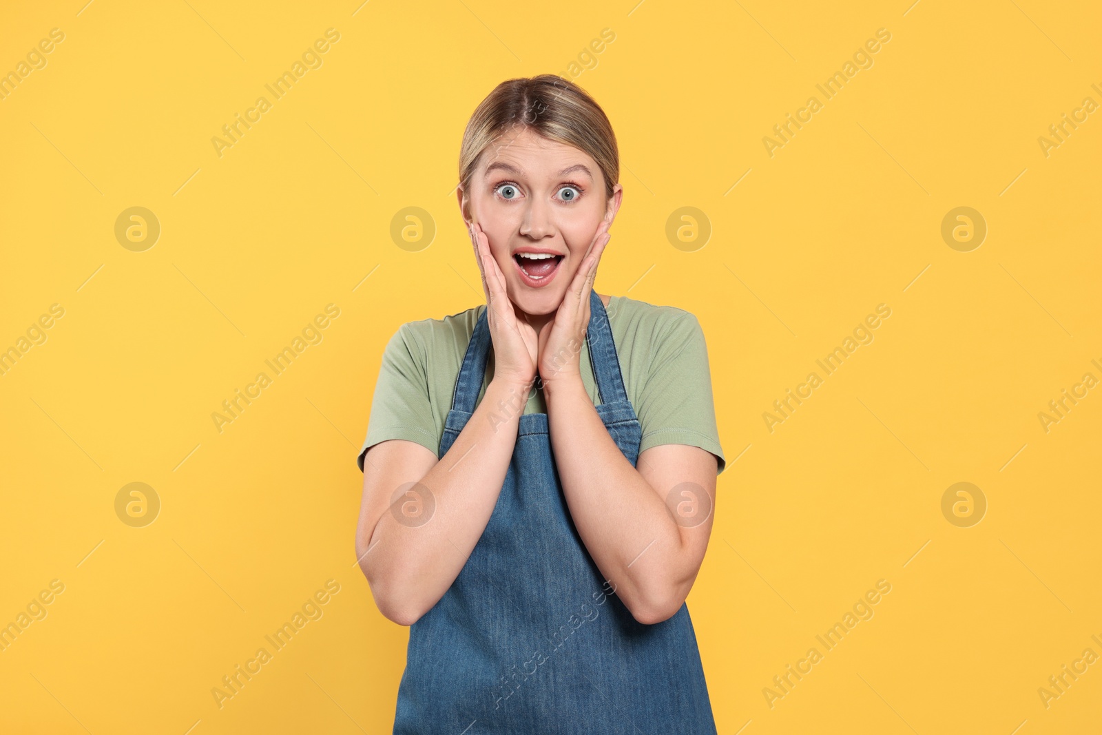 Photo of Beautiful young woman in denim apron on orange background