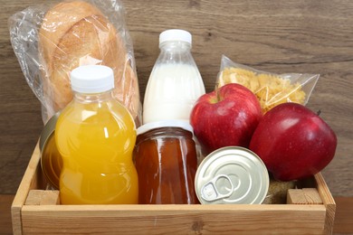 Photo of Humanitarian aid. Different food products for donation in crate on wooden table, closeup