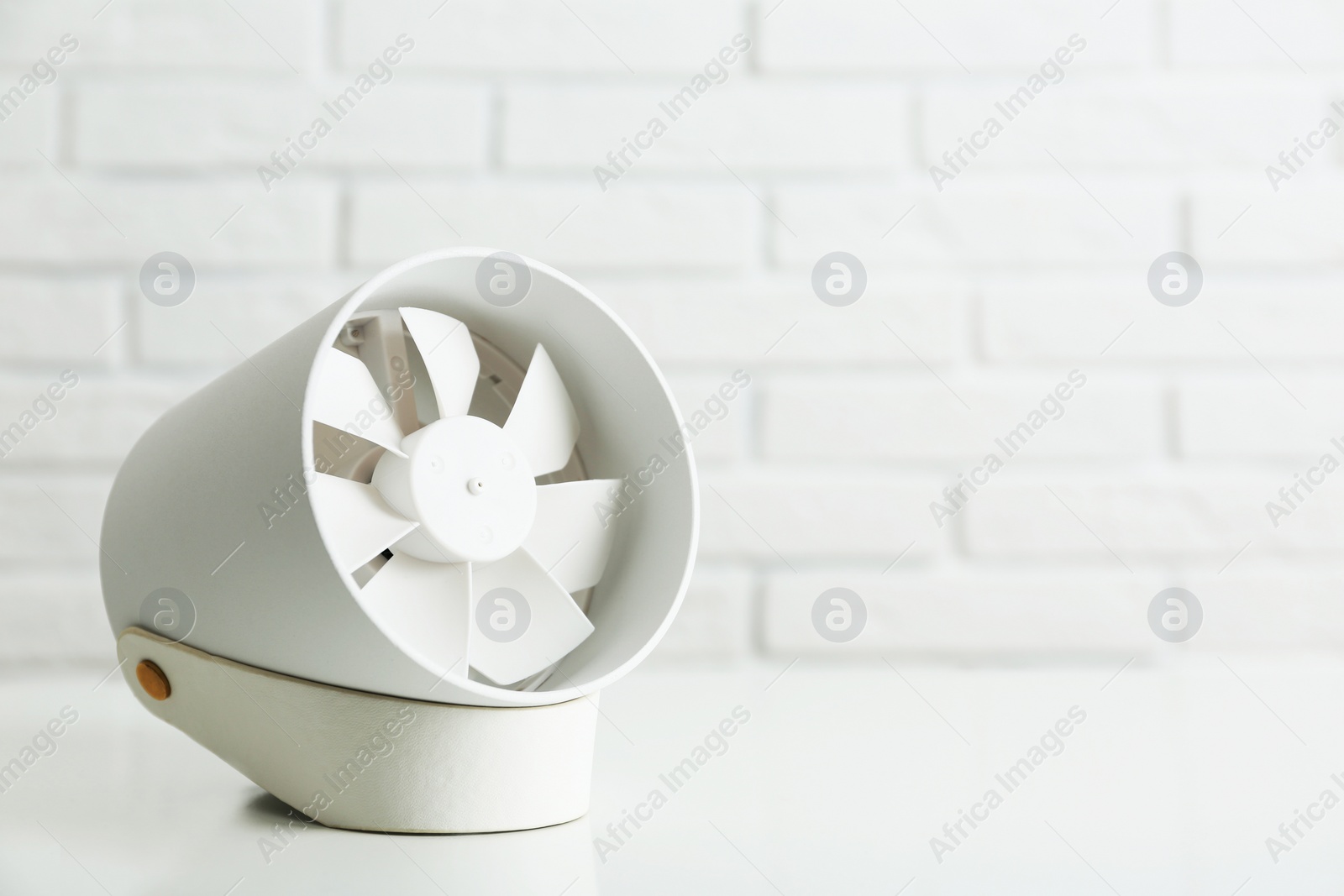 Photo of Portable fan on table near white brick wall, space for text. Summer heat