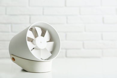 Portable fan on table near white brick wall, space for text. Summer heat