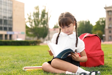 Schoolgirl with stationery sitting on grass outdoors