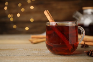 Glass cup of hot tea with aromatic cinnamon on wooden table against blurred lights. Space for text