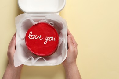 Woman holding takeaway box with bento cake at beige table, top view. St. Valentine's day surprise