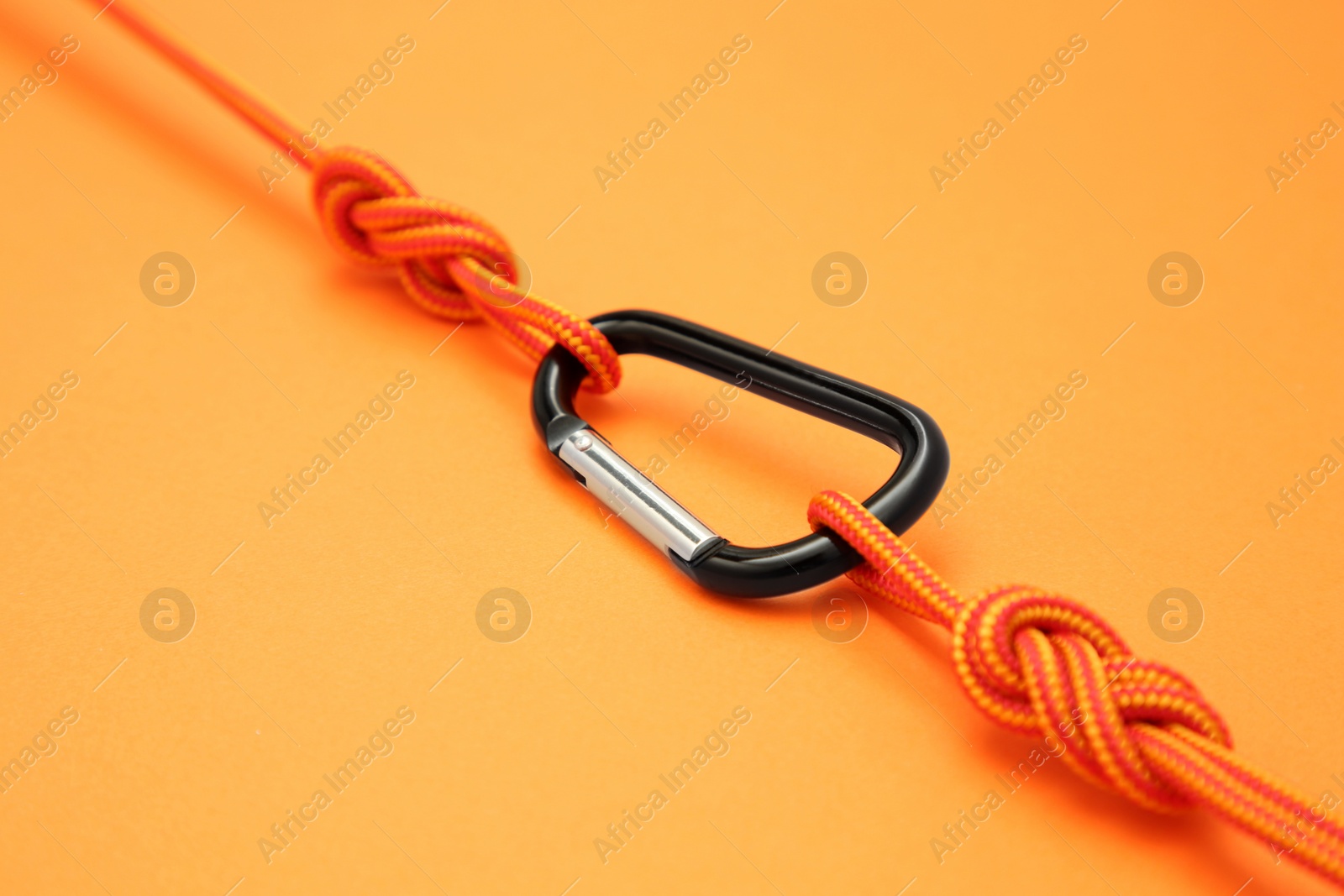 Photo of One metal carabiner with ropes on orange background, closeup