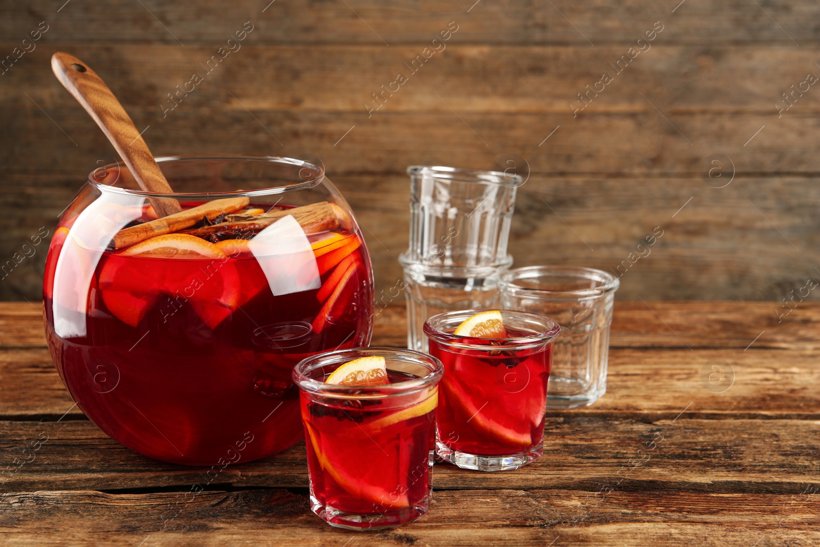 Photo of Bowl of delicious aromatic punch drink and glasses on wooden table. Space for text