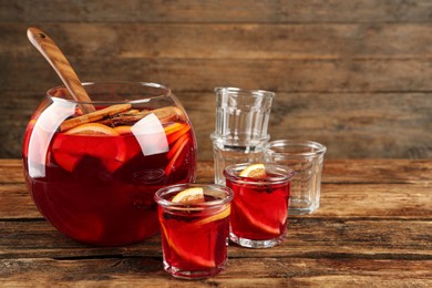 Photo of Bowl of delicious aromatic punch drink and glasses on wooden table. Space for text