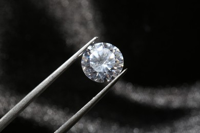 Photo of Tweezers with beautiful shiny diamond on dark background, closeup