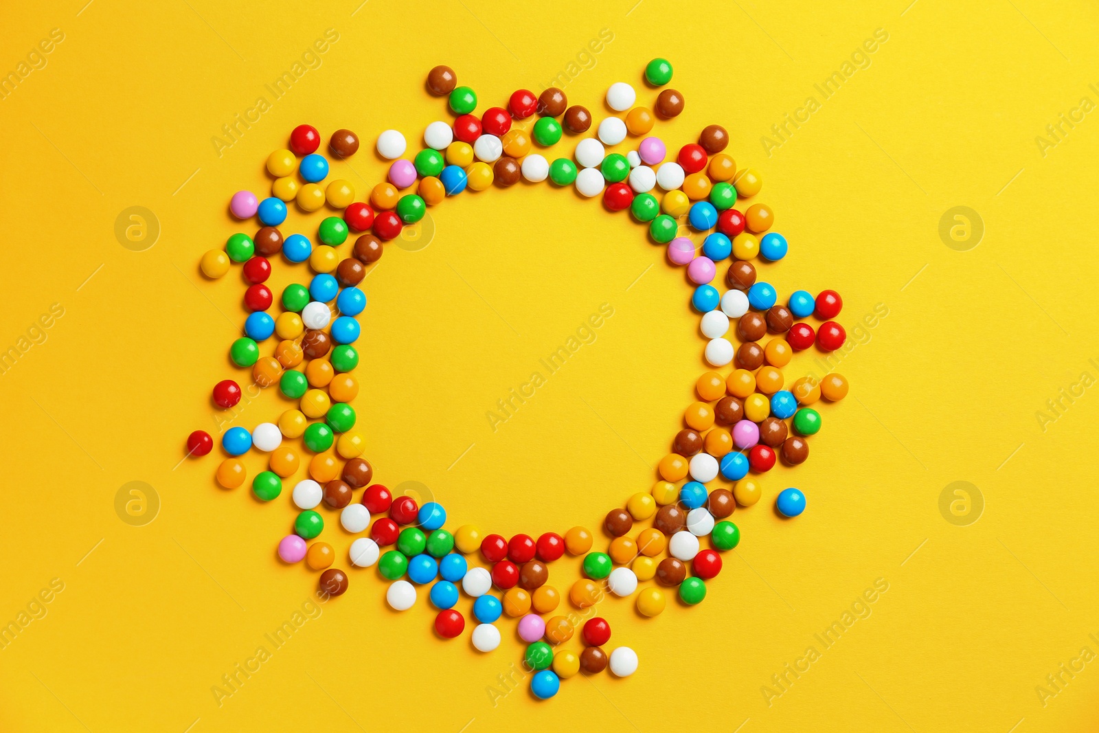 Photo of Frame made of delicious glazed candies on yellow background, top view. Space for text