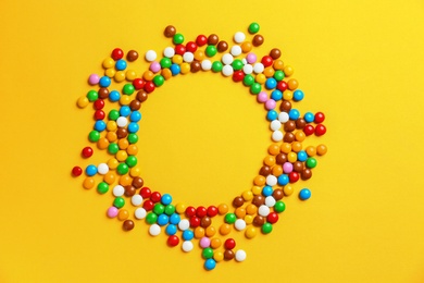 Photo of Frame made of delicious glazed candies on yellow background, top view. Space for text