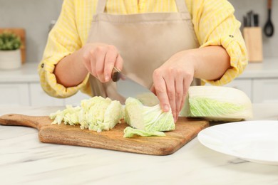 Photo of Woman cutting fresh chinese cabbage at table in kitchen, closeup