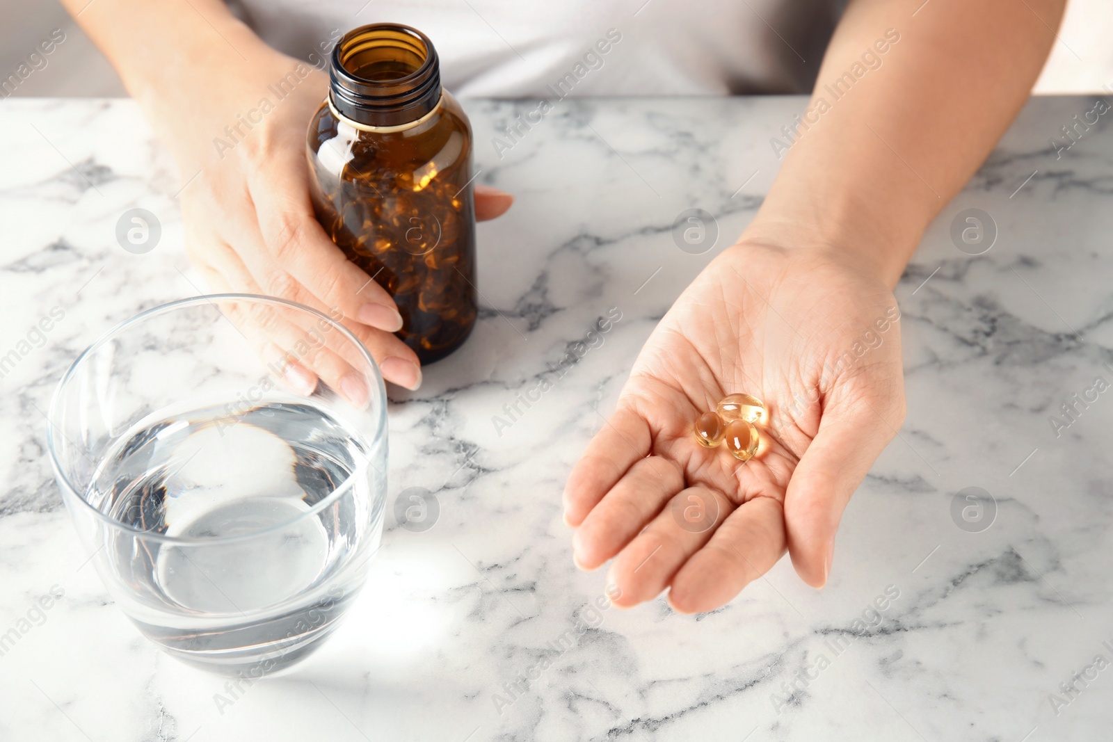 Photo of Woman with fish oil pills at table, closeup