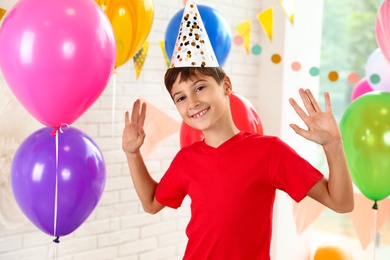 Happy boy near bright balloons at birthday party indoors