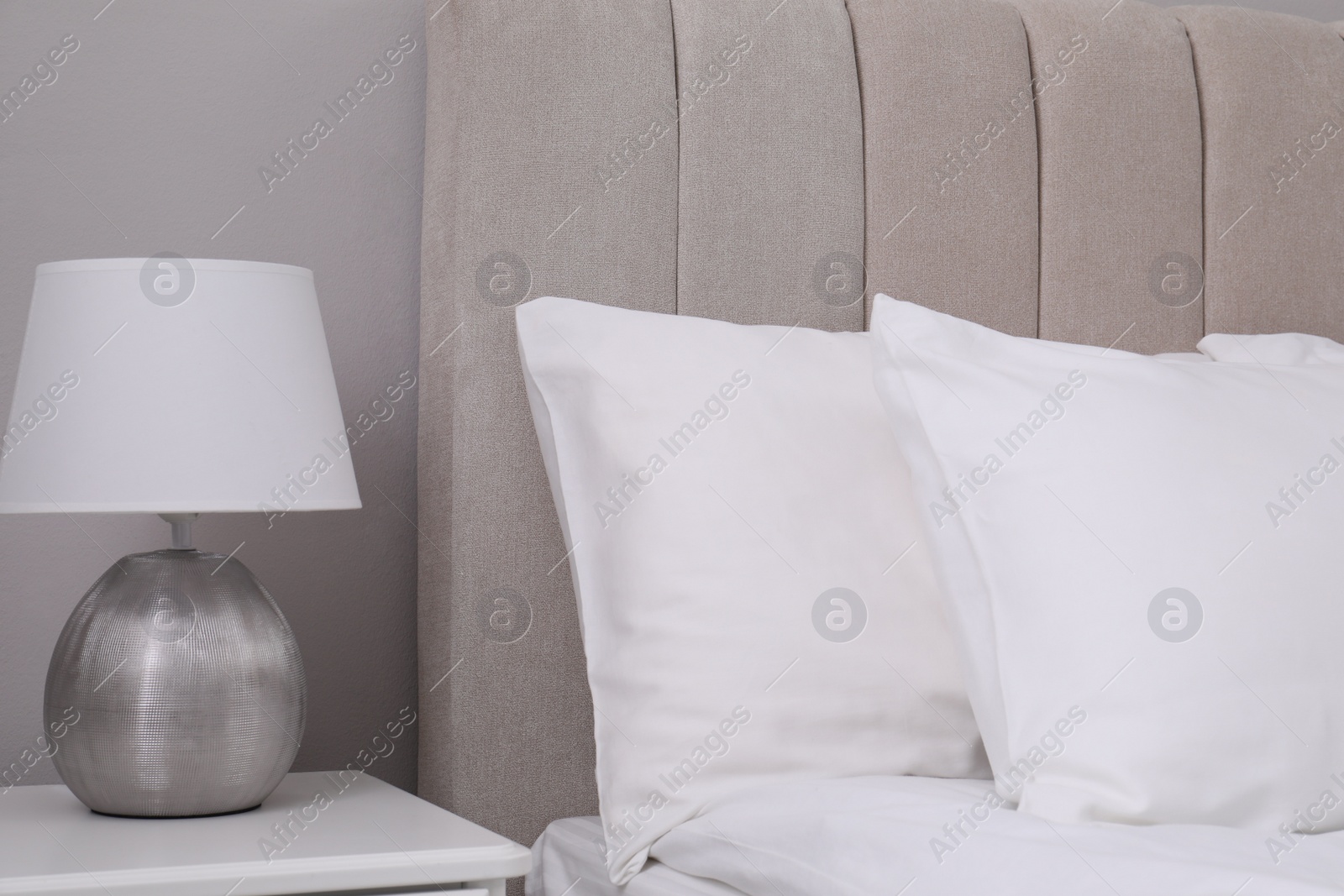 Photo of White soft pillows on bed and lamp in room