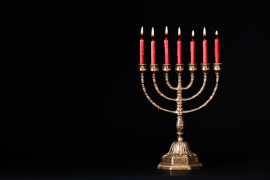 Photo of Golden menorah with burning candles on black background, space for text