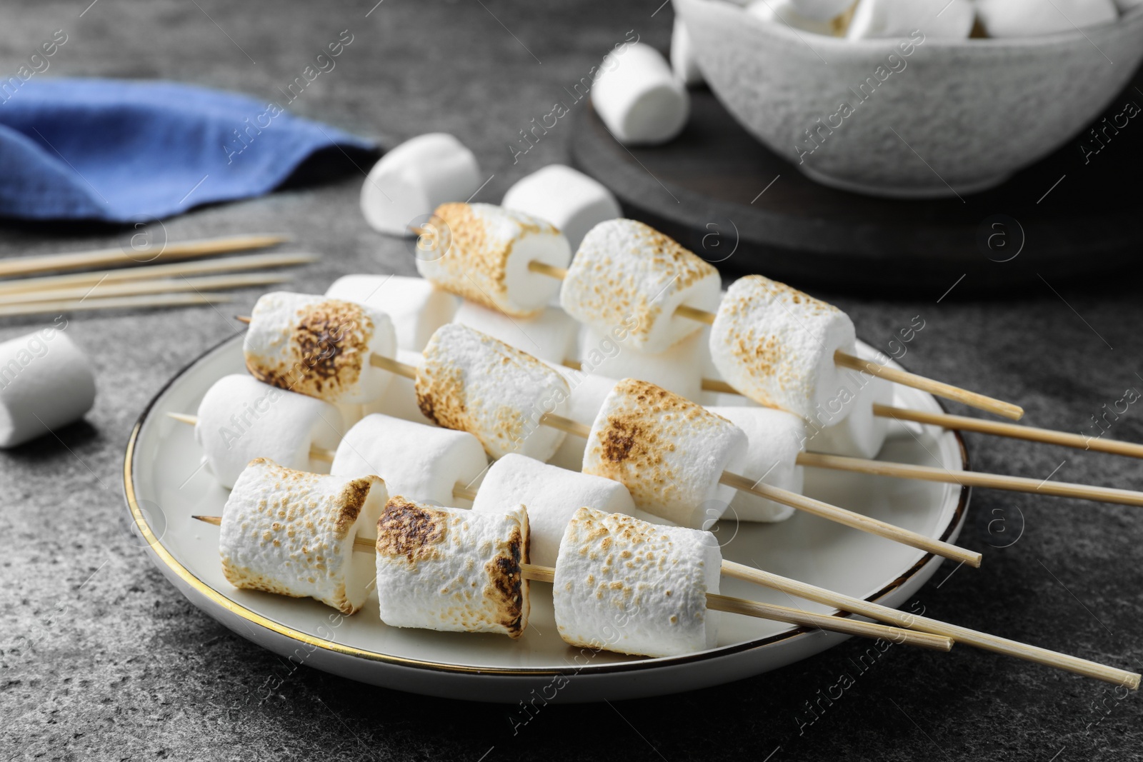 Photo of Sticks with roasted marshmallows on grey table