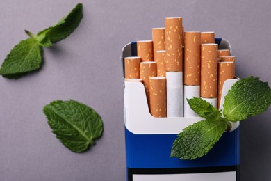 Photo of Pack of menthol cigarettes and mint leaves on grey background, flat lay