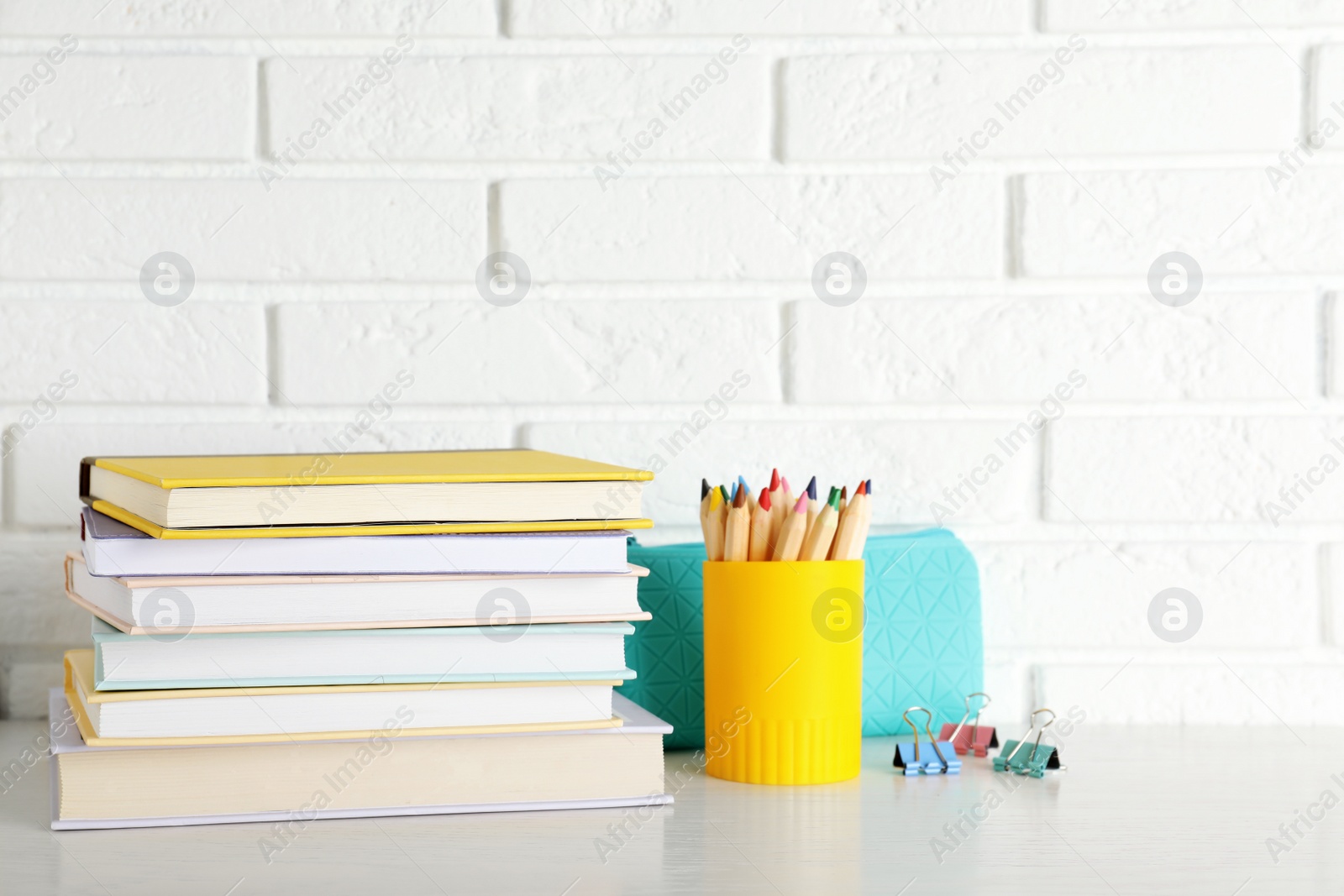 Photo of Stack of hardcover books and stationery on table against brick wall. Space for text