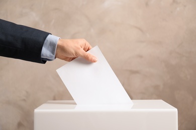 Photo of Man putting his vote into ballot box on color background, closeup