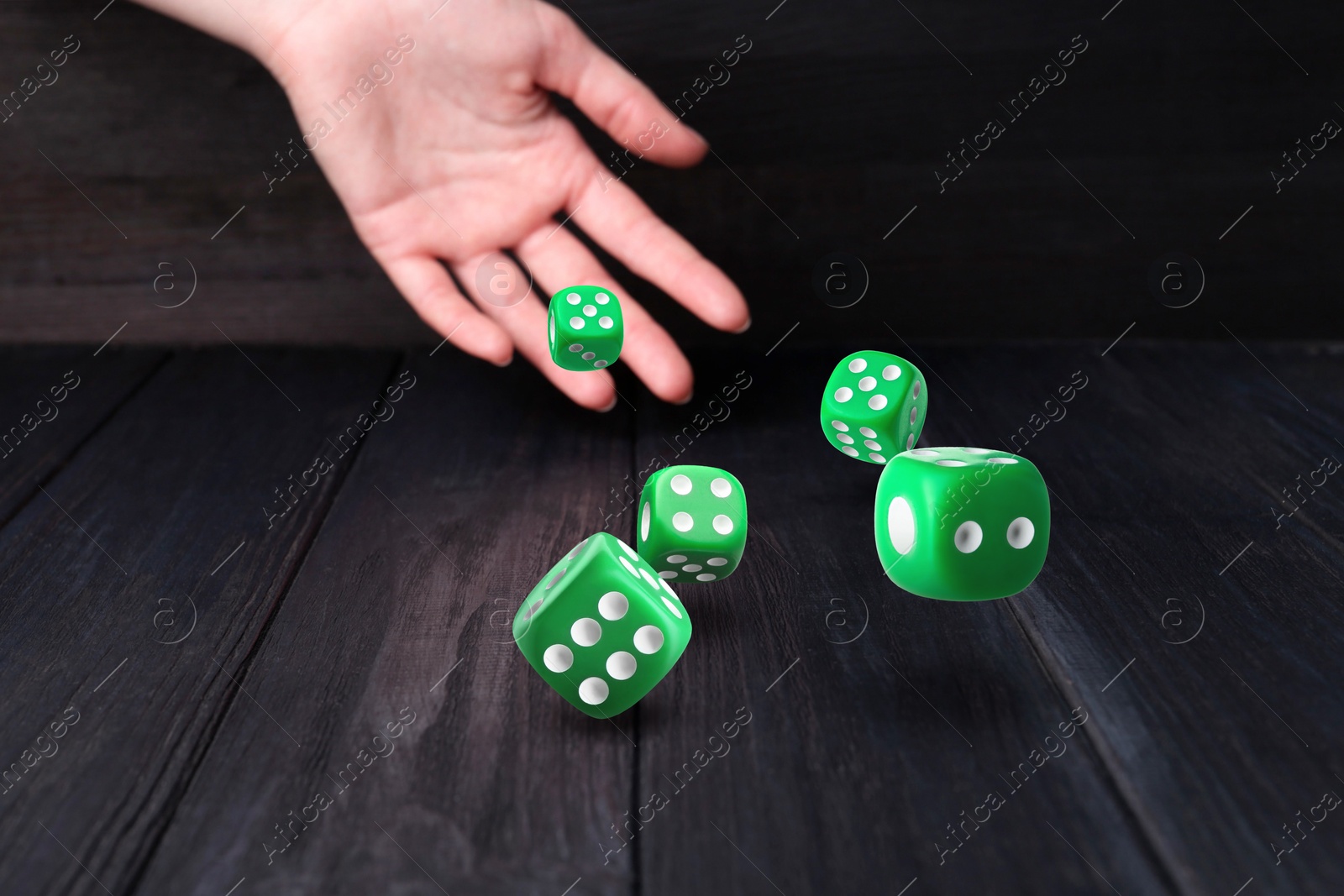 Image of Woman throwing green dice on black wooden table, closeup