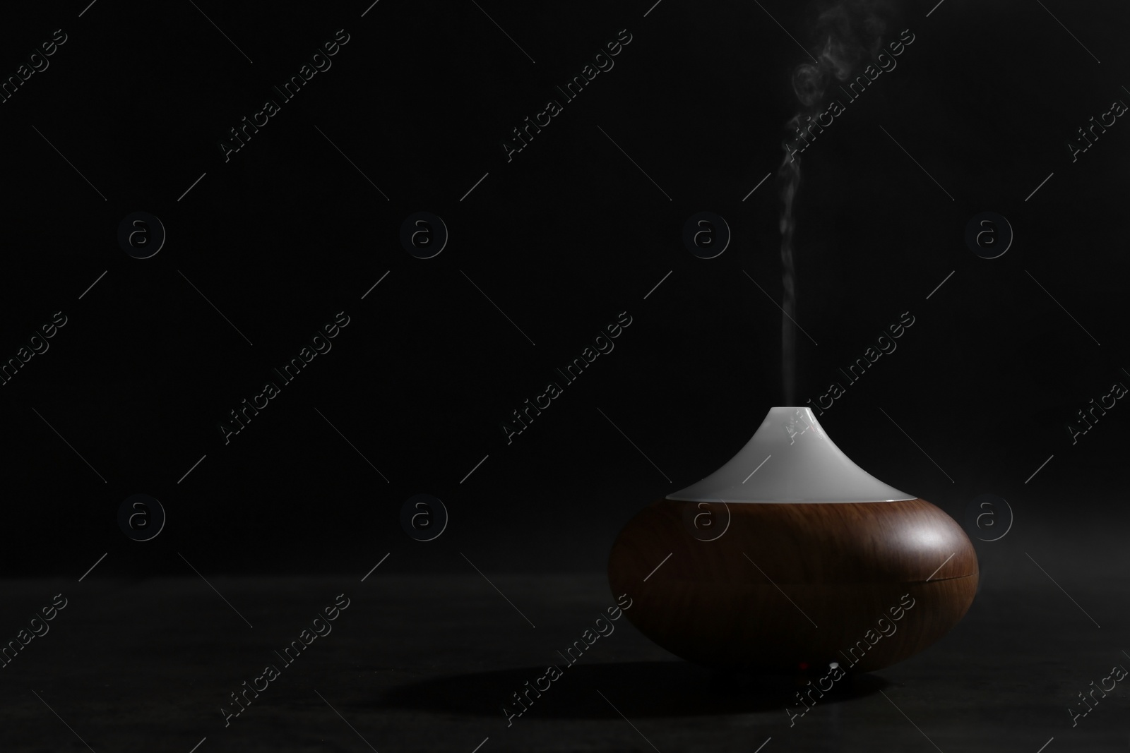 Photo of Aroma oil diffuser on table against dark background. Space for text