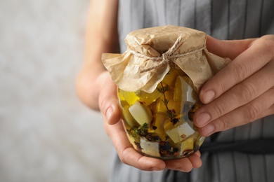 Photo of Woman holding jar with pickled feta cheese on beige background, closeup. Space for text