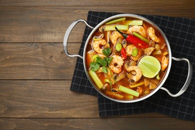 Photo of Saucepan with delicious Tom Yum soup on wooden table, top view. Space for text